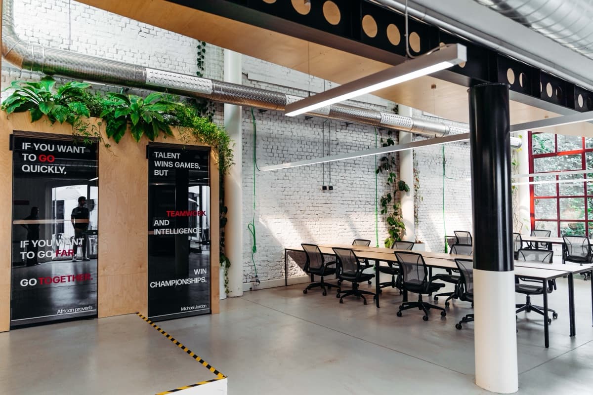 Open space del coworking WAO, con lunga scrivania condivisa e muro in mattoni bianchi