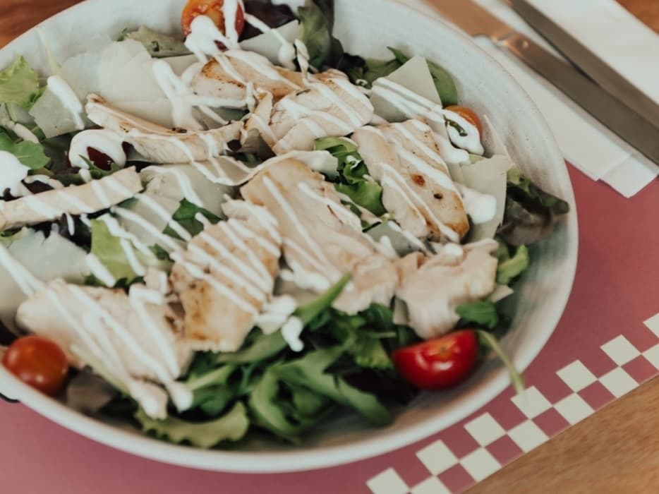 A salad with grilled chicken and cherry tomatoes served at a WAO Kitchen table