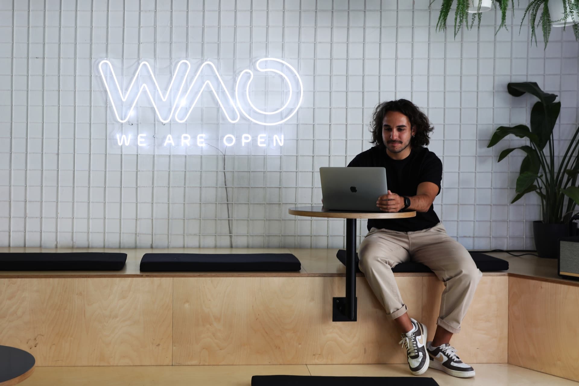 Ragazzo al laptop sulla gradinata, sotto l'insegna al neon WAO